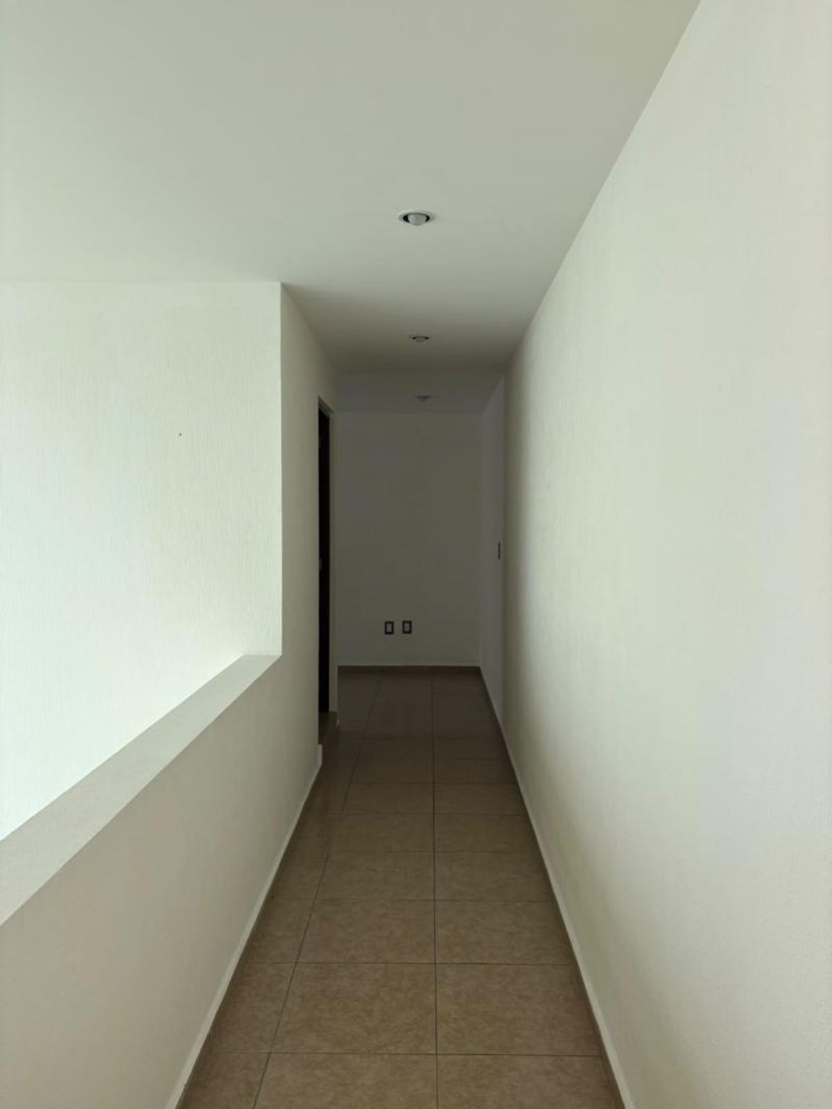 Pasillo interior con muros blancos, piso cerámico beige y luces empotradas en el techo