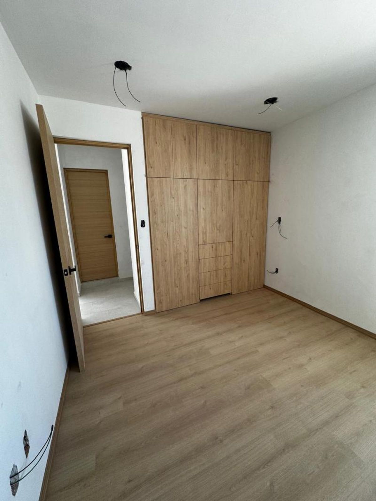 Habitación vacía con piso de madera clara, clóset empotrado de madera y paredes blancas