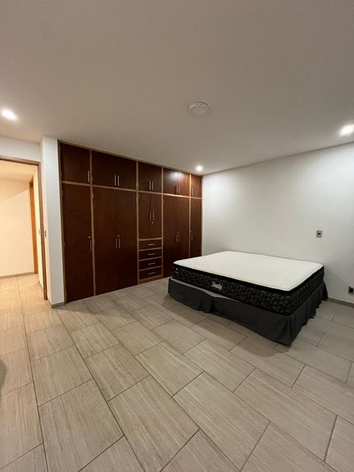 Recámara con piso de cerámica clara, cama y clóset empotrado de madera oscura