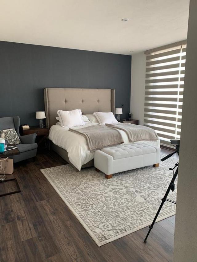 Recámara con pared de acento gris, cama tapizada, banca blanca y piso de madera