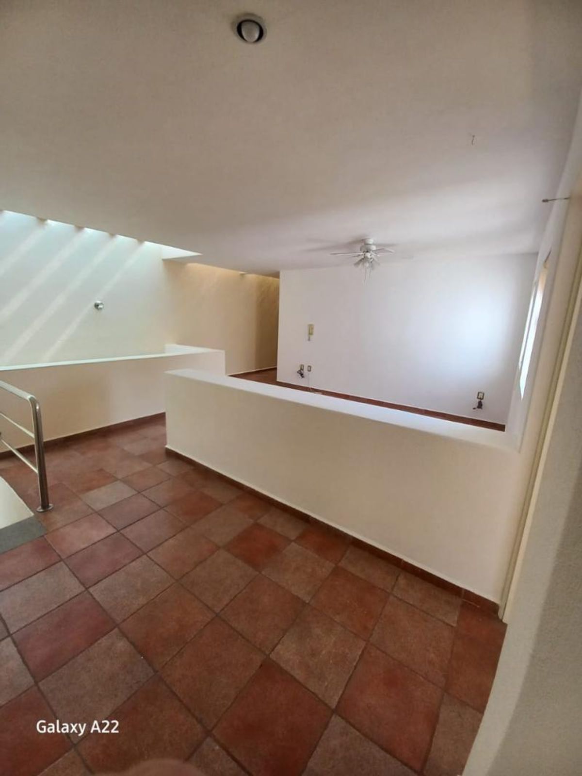 Pasillo superior con piso de cerámica terracota, murete blanco, tragaluz y ventilador de techo