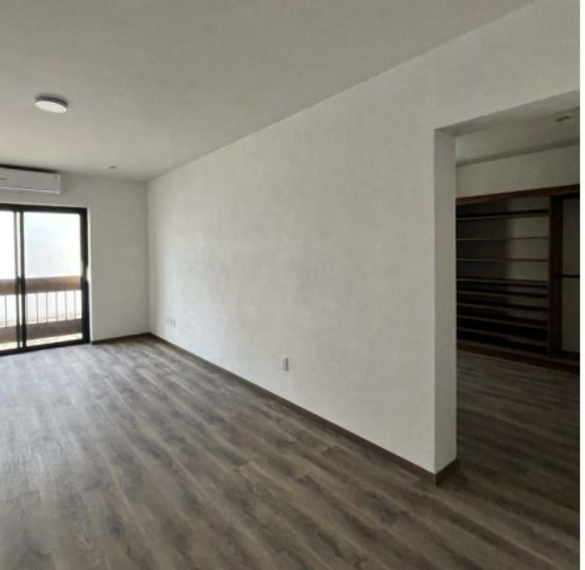Habitación vacía con piso tipo madera, paredes blancas, puerta corrediza de cristal y vestidor