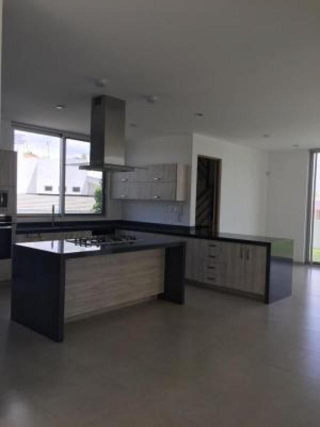 Cocina con isla central, cubiertas oscuras, campana de acero inoxidable y gabinetes de madera