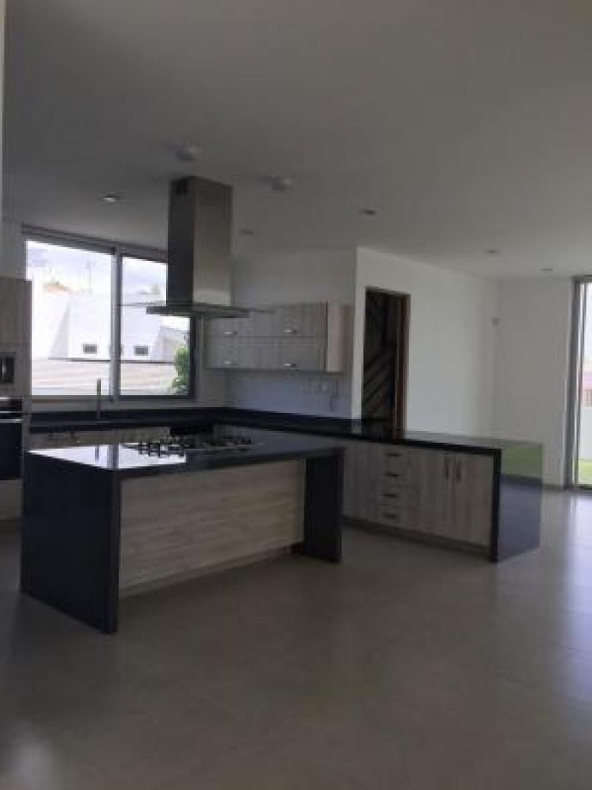 Cocina con isla central, cubiertas oscuras, campana de acero inoxidable y gabinetes de madera