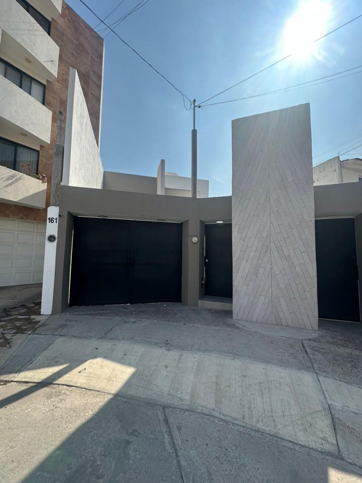 Fachada moderna con portones negros, muro decorativo de piedra clara y número exterior 161