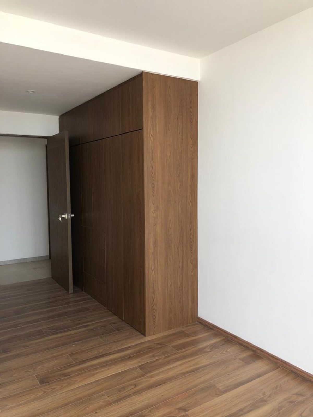 Habitación con piso laminado de madera, paredes blancas y clóset empotrado de madera