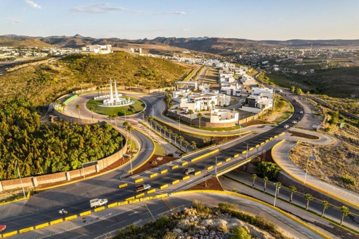 Vista aérea de fraccionamiento residencial con glorieta, paso a desnivel, palmeras y casas blancas