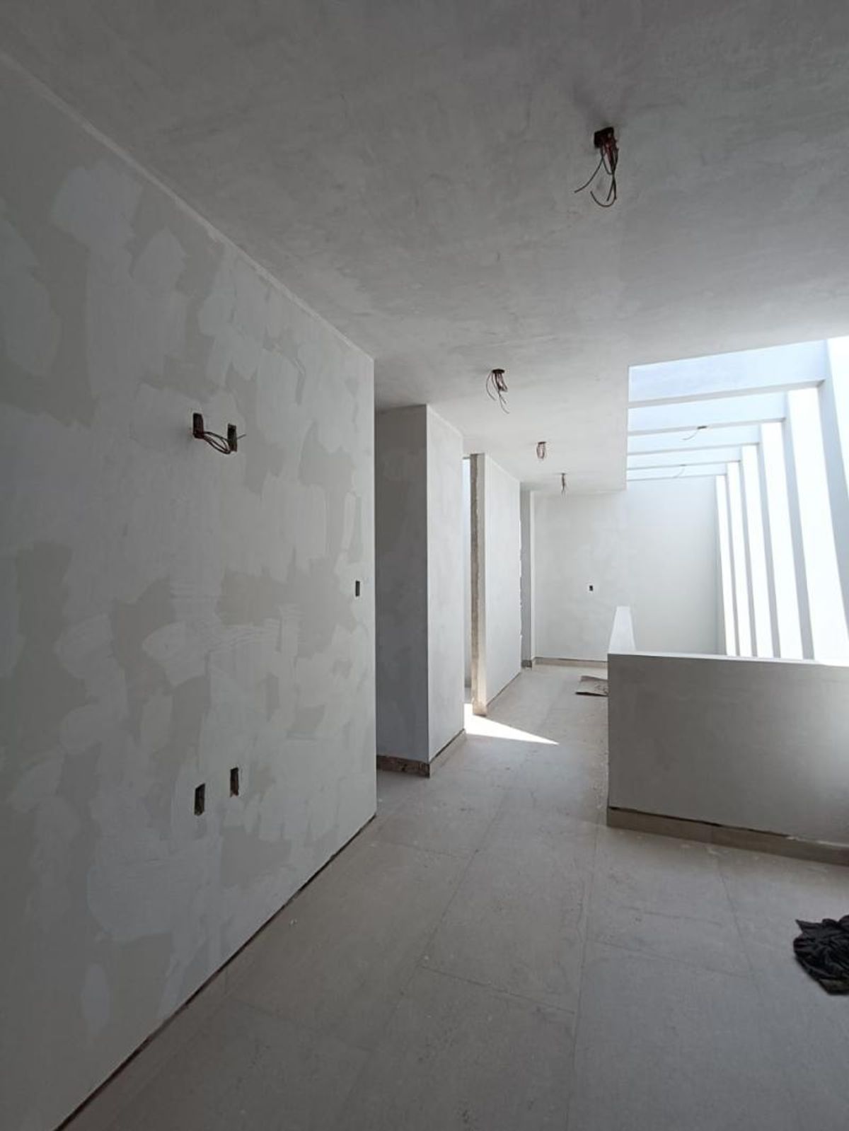 Pasillo interior con paredes enyesadas, cableado eléctrico expuesto, piso cerámico gris e iluminación natural