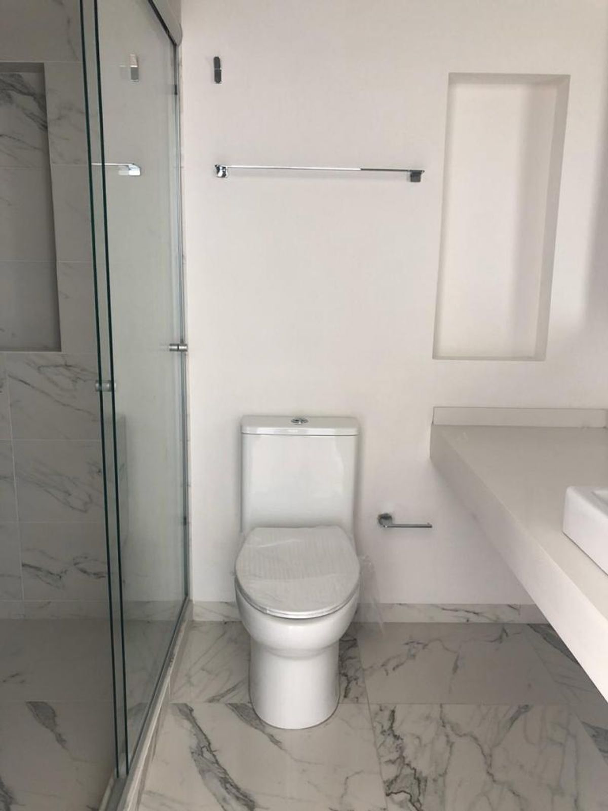 Baño con inodoro blanco, cancel de cristal en regadera y piso cerámico tipo mármol