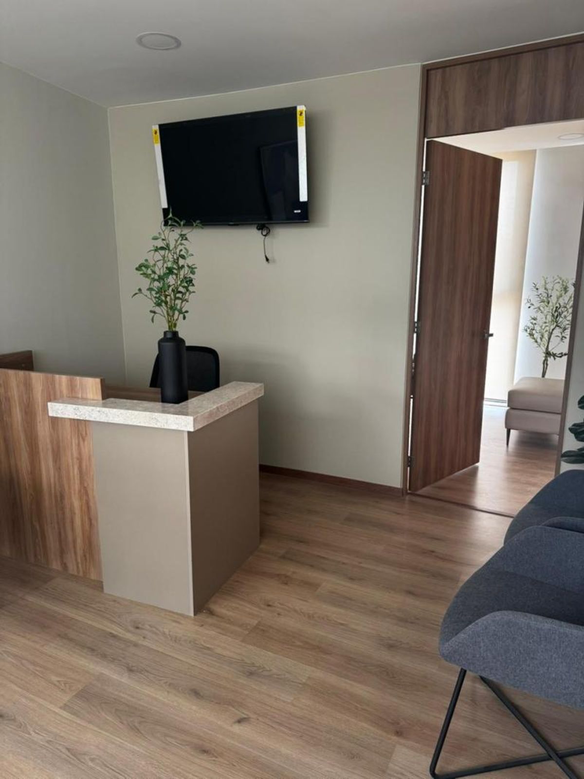 Recepción con mostrador de madera, piso laminado, televisión en pared y sillas de espera