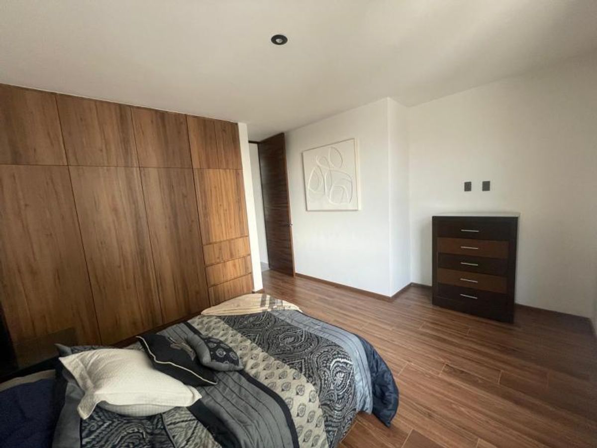 Dormitorio con clóset de madera, piso acabado madera, cómoda oscura y cama vestida