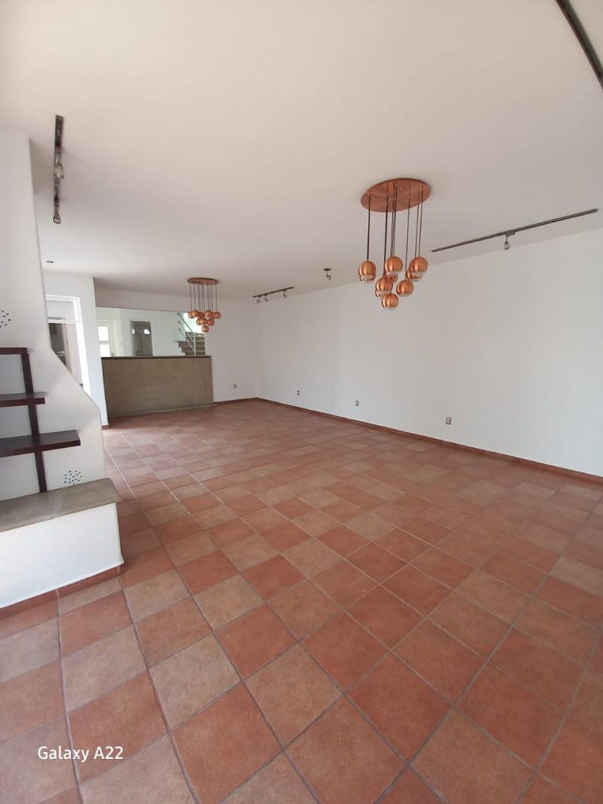Habitación vacía con paredes blancas, piso de loseta rojiza y lámparas colgantes de cobre