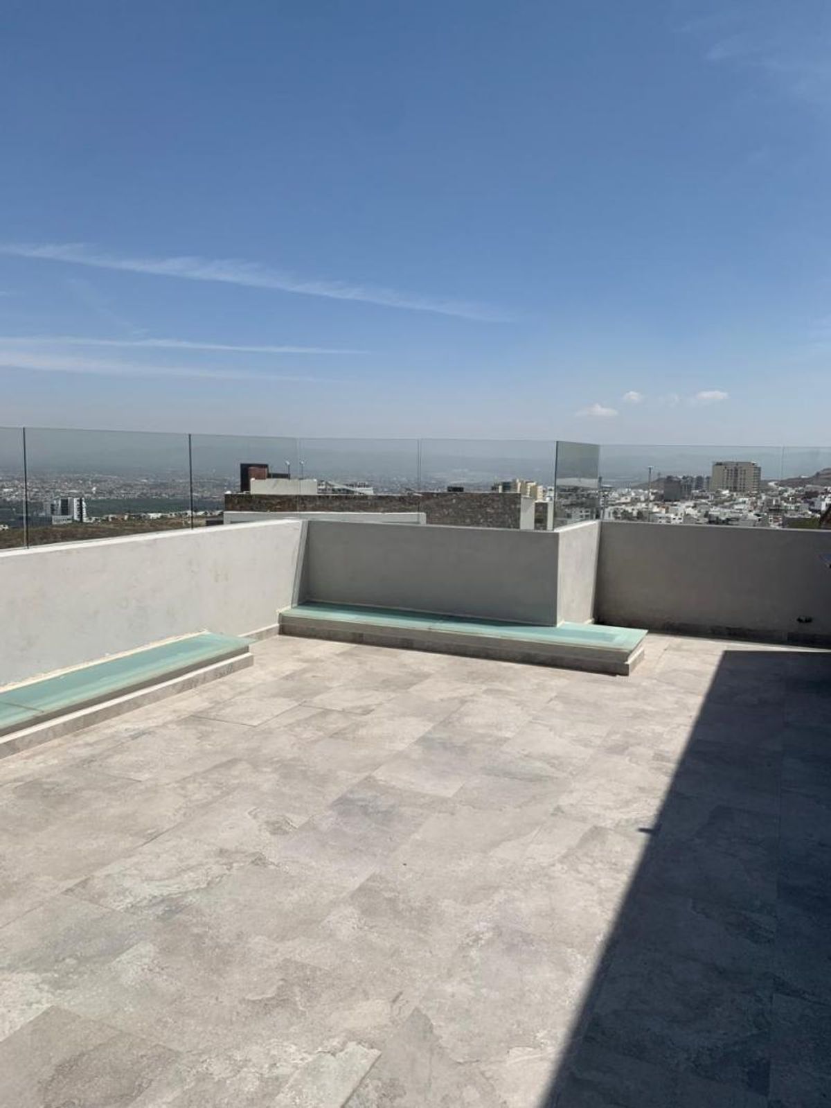 Terraza con piso de loseta gris, bancas de concreto, barandal de cristal y vista panorámica