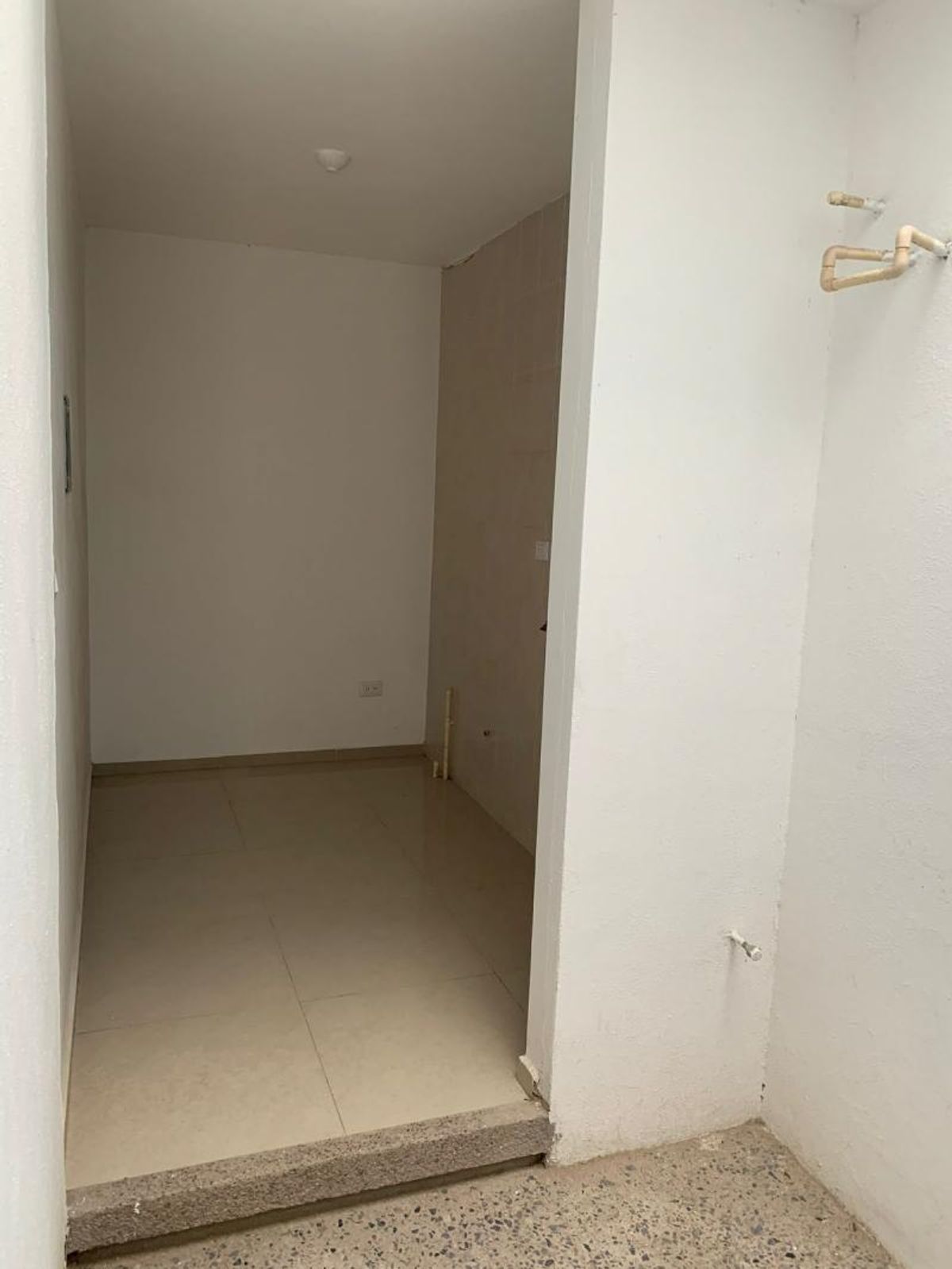 Espacio pequeño de servicio con piso de cerámica clara, paredes blancas y tuberías expuestas