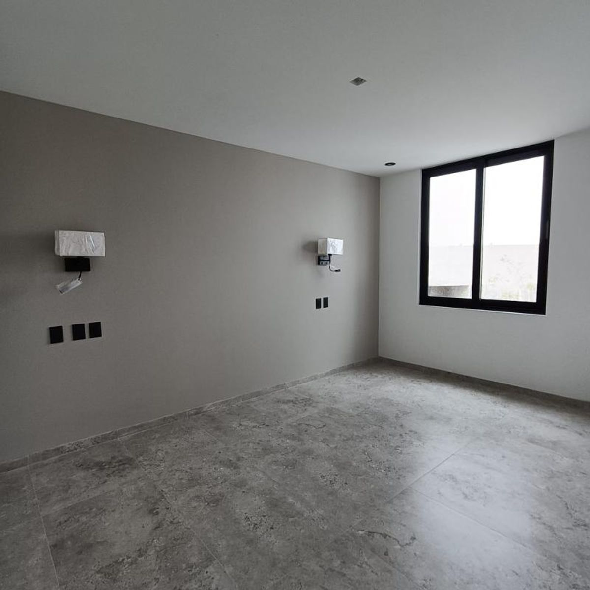 Recámara vacía con piso cerámico gris, apliques de pared y ventana con marco negro