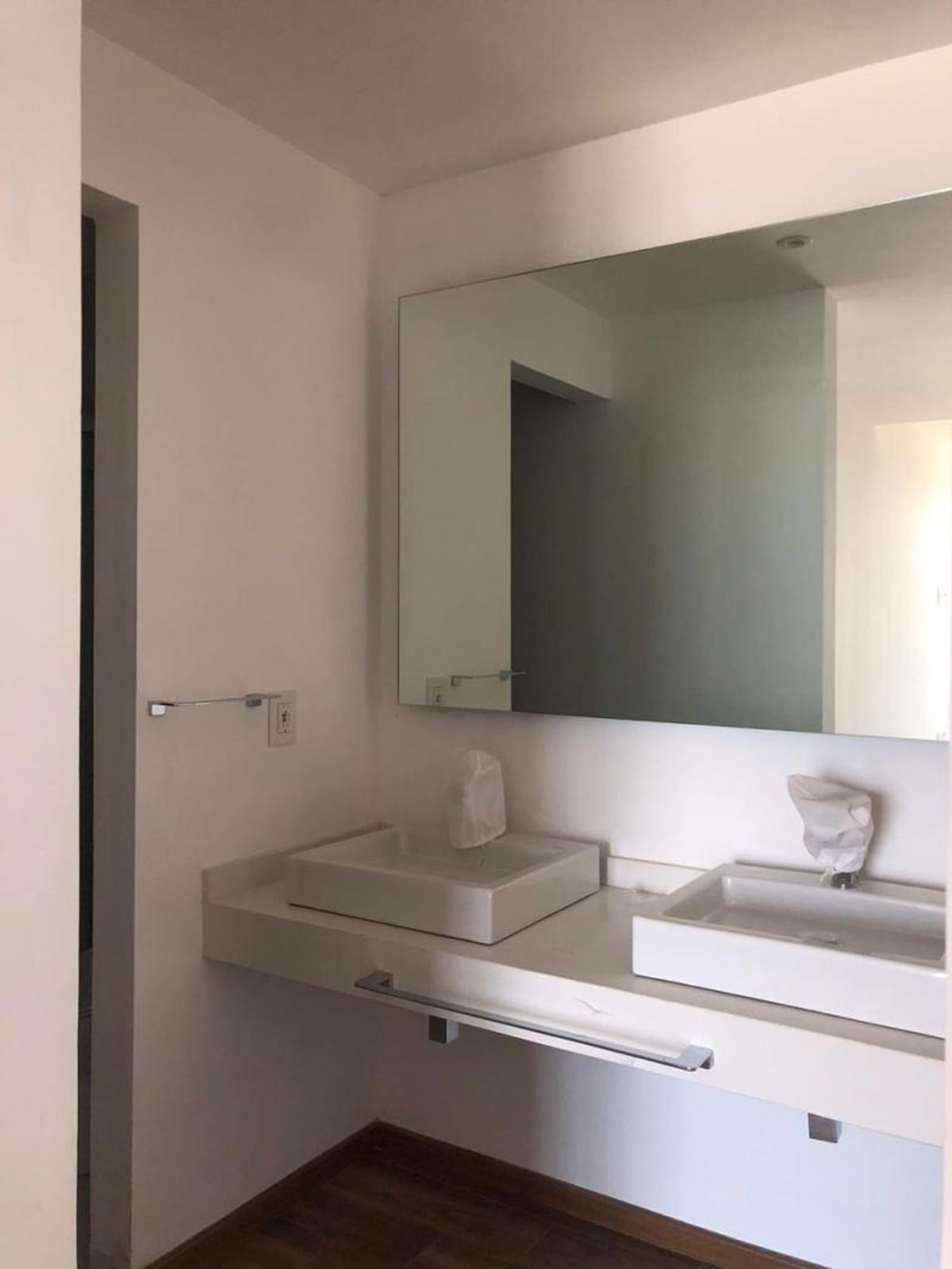 Baño con cubierta flotante blanca, dos lavabos rectangulares, espejo amplio y piso de madera