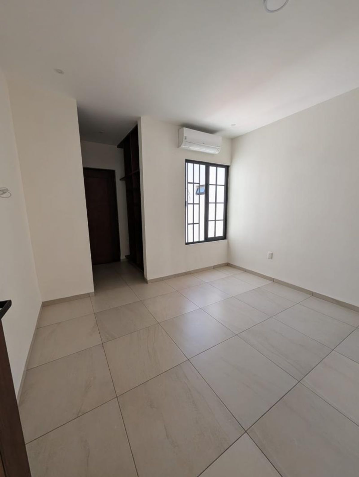 Recámara vacía con piso de azulejo claro, ventana con marco negro y minisplit