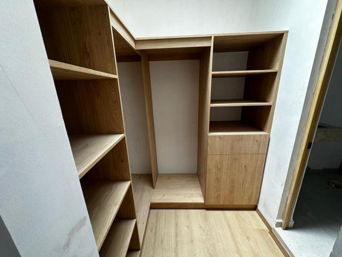 Vestidor de madera clara con repisas, cajones, espacio para colgar y piso laminado