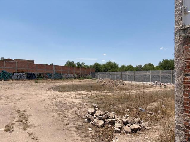 Terreno plano de tierra con escombros, delimitado por bardas perimetrales de ladrillo y concreto