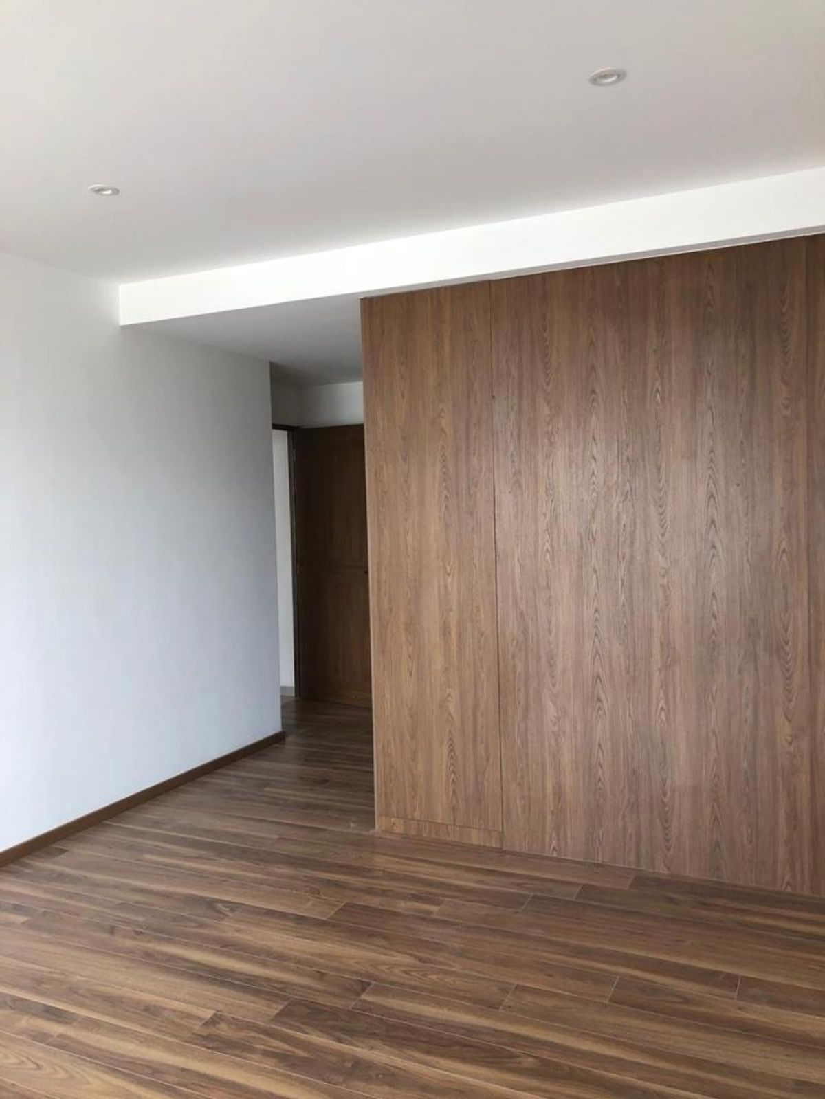 Espacio interior vacío con piso de madera, paredes blancas y panelado de madera