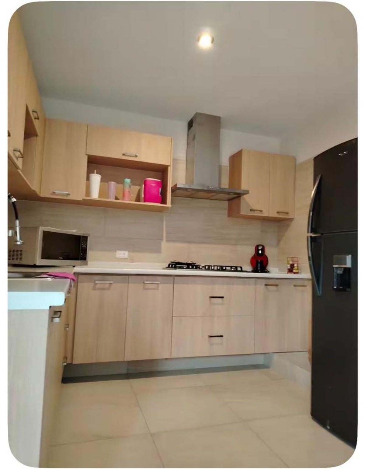 Cocina integral con gabinetes de madera clara, campana de acero inoxidable y refrigerador negro