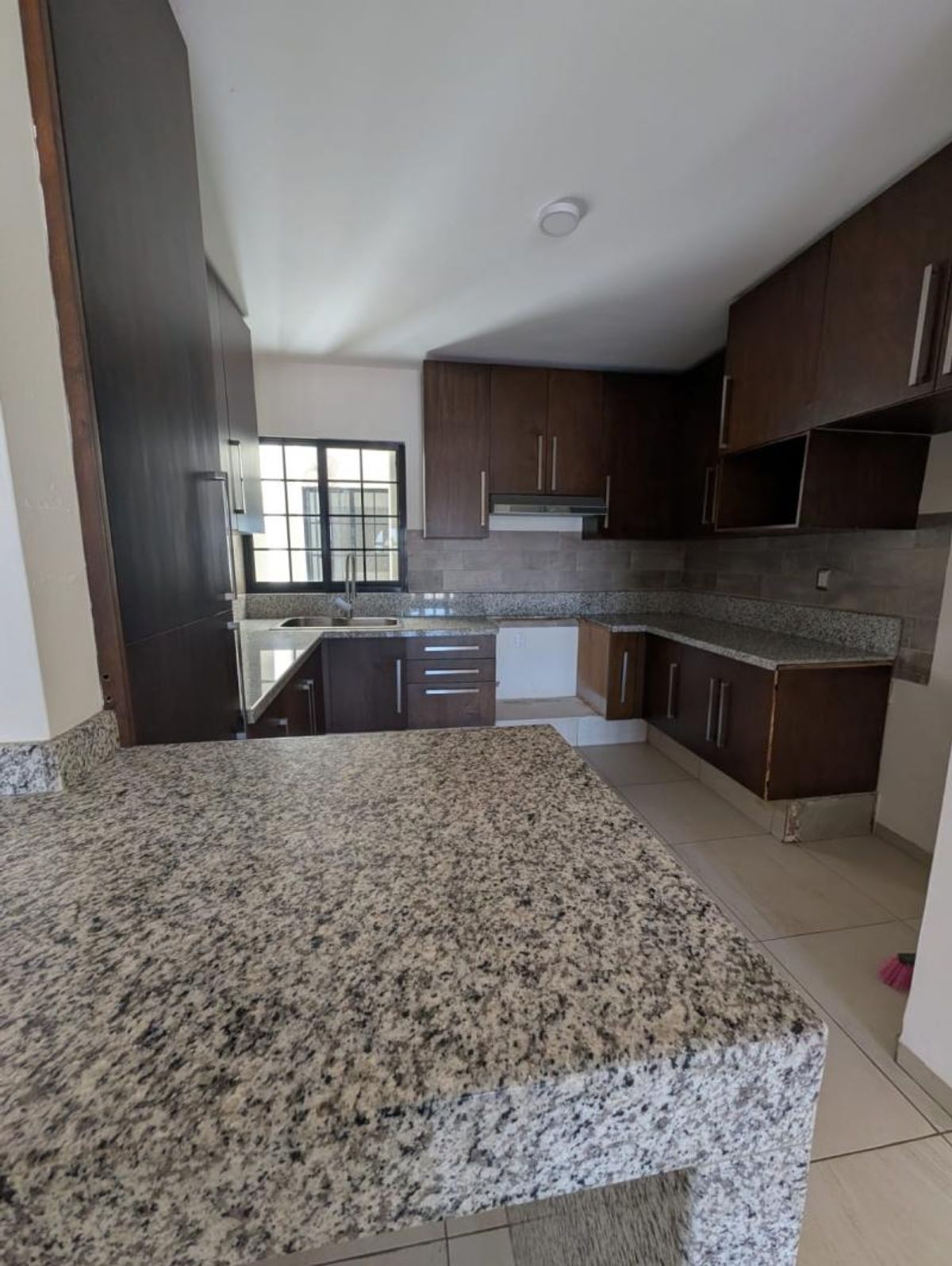 Cocina integral con cubiertas de granito, gabinetes de madera oscura, tarja y piso claro