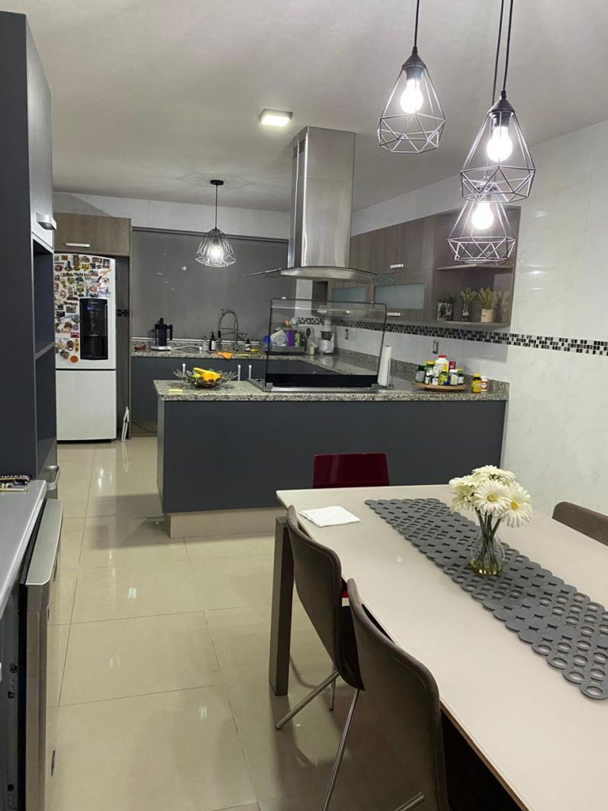 Cocina abierta con barra de granito, campana de acero inoxidable y mesa de comedor