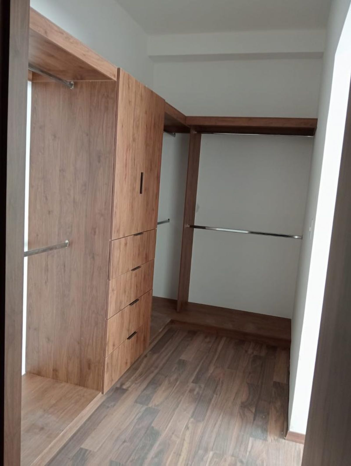 Vestidor de madera con cajonera, barras metálicas para colgar ropa y piso laminado