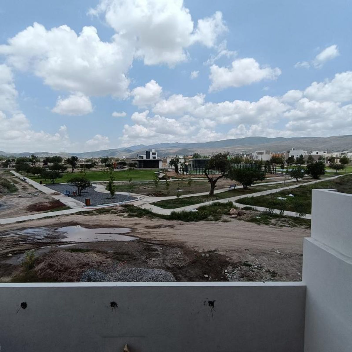 Vista desde balcón hacia parque con áreas verdes, senderos, árboles y montañas al fondo