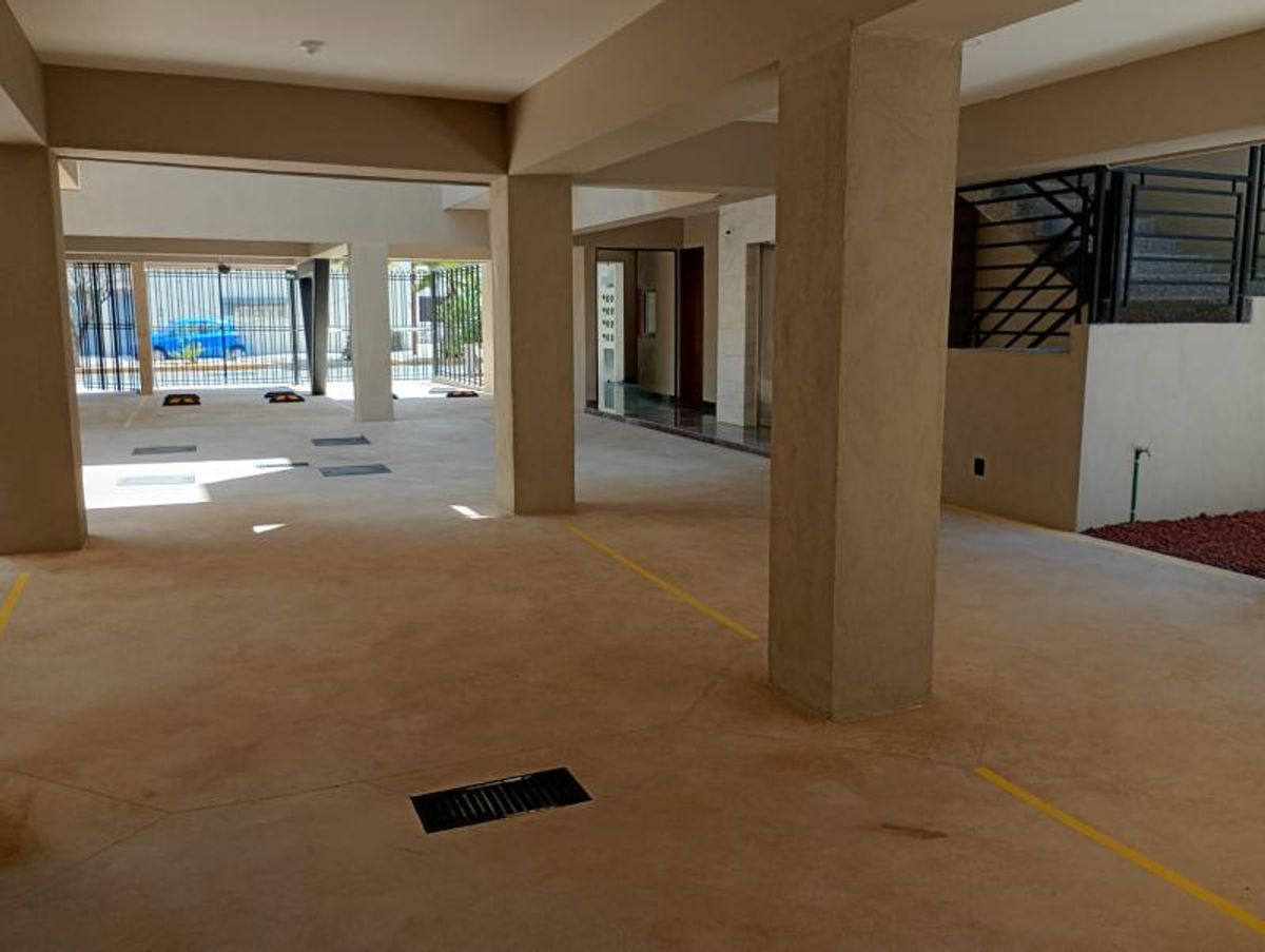 Estacionamiento techado con columnas de concreto, cajones delimitados con líneas amarillas y rejilla metálica