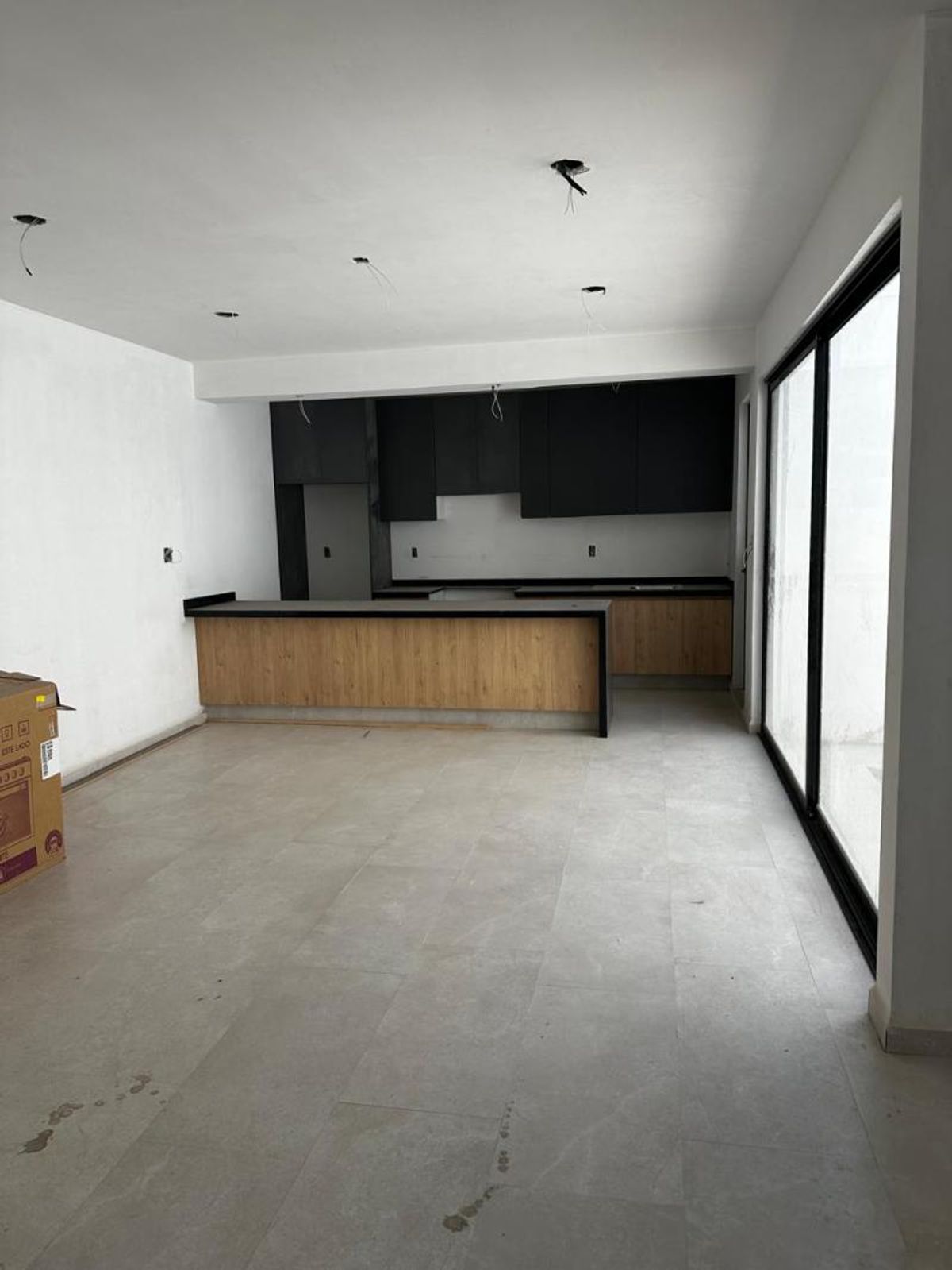 Cocina abierta con barra de madera, cubierta negra, gabinetes superiores oscuros y piso claro