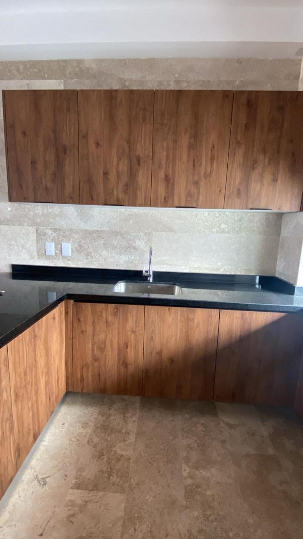 Cocina con gabinetes de madera, cubierta de granito negro, tarja de acero y piso beige