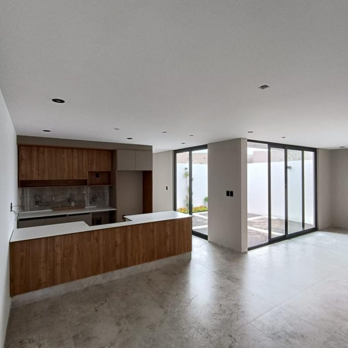 Cocina abierta con barra de madera, cubierta blanca y ventanales hacia el patio