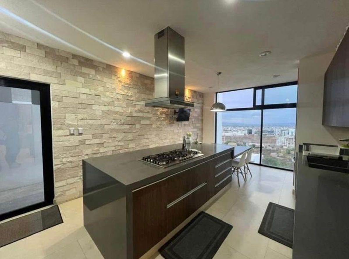 Cocina moderna con isla central, pared de piedra, campana de acero y ventanal panorámico
