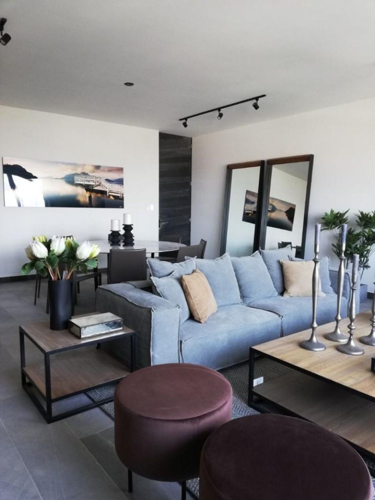 Sala con sofá gris claro, taburetes de terciopelo, mesa de madera y comedor al fondo