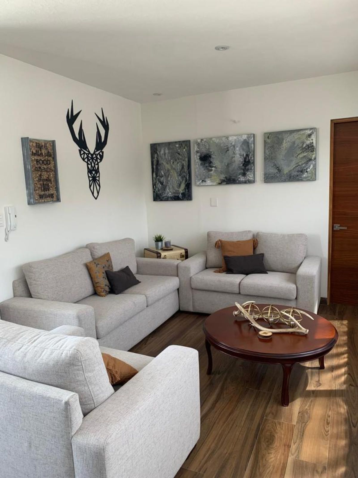Sala con sofás grises, mesa de centro redonda de madera y cuadros decorativos