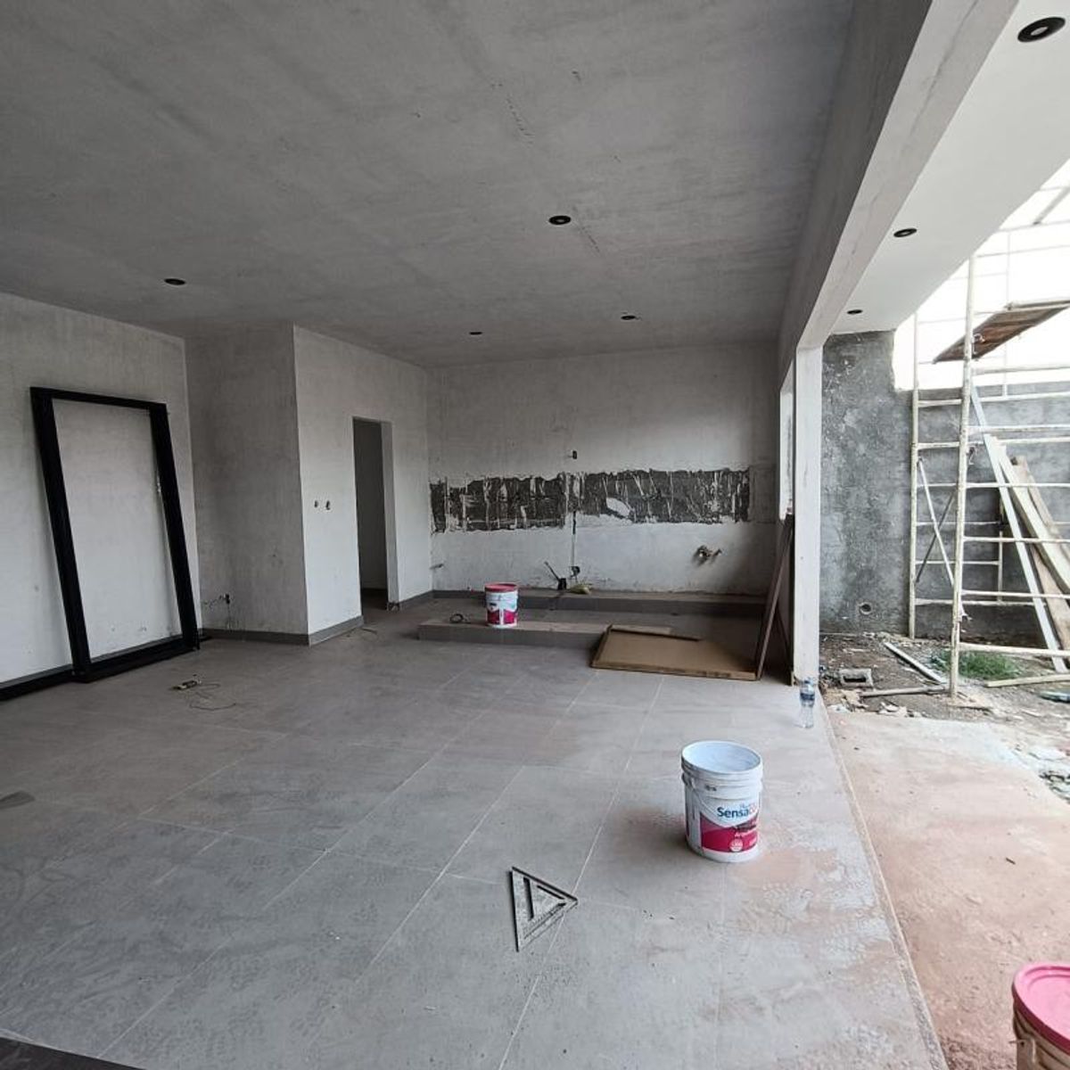 Espacio interior en acabados con piso gris, paredes de yeso y cubetas de pintura