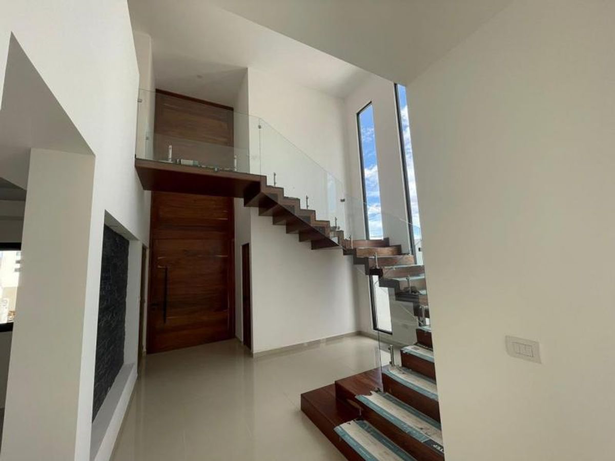 Vestíbulo de doble altura con escalera flotante de madera y barandal de cristal