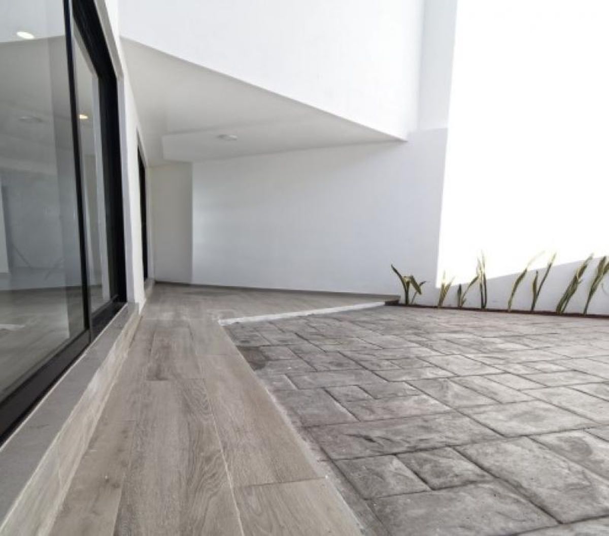 Patio exterior con piso tipo madera, concreto estampado gris, ventanal y pequeñas plantas