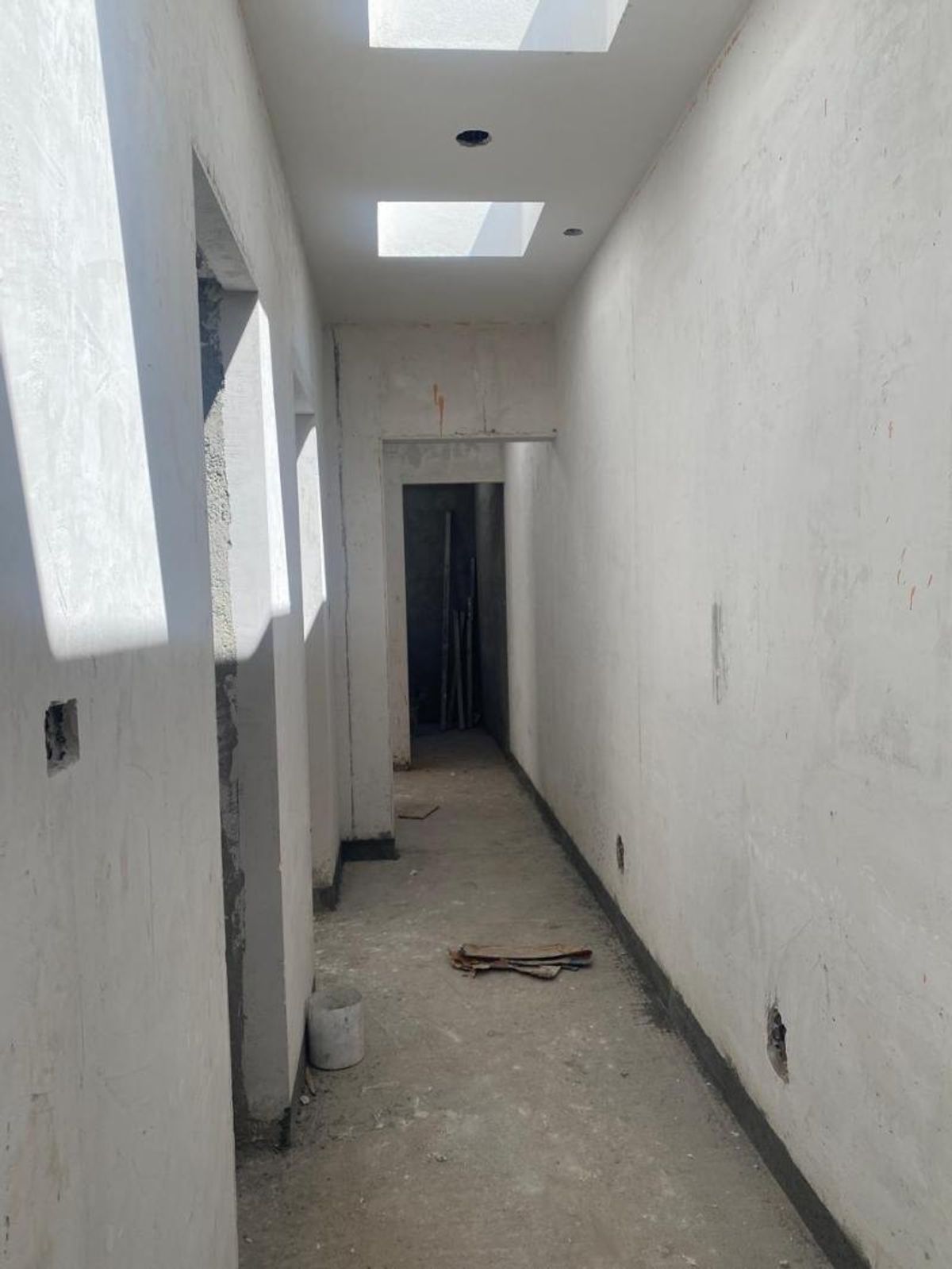 Pasillo en construcción con tragaluces en el techo, muros blancos y piso de concreto