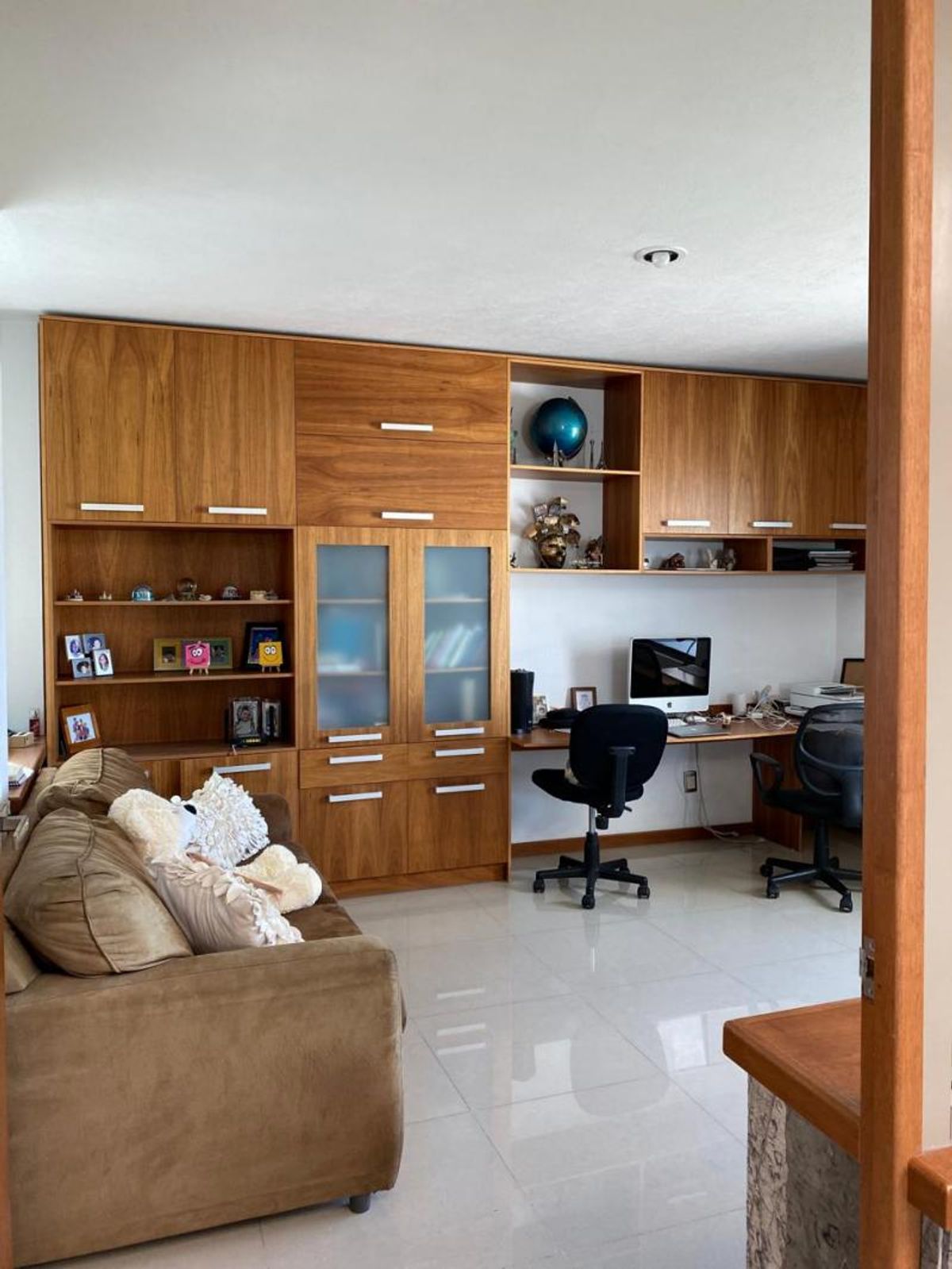Estudio con amplio mueble de madera, escritorio, sillas giratorias, sofá café y piso cerámico