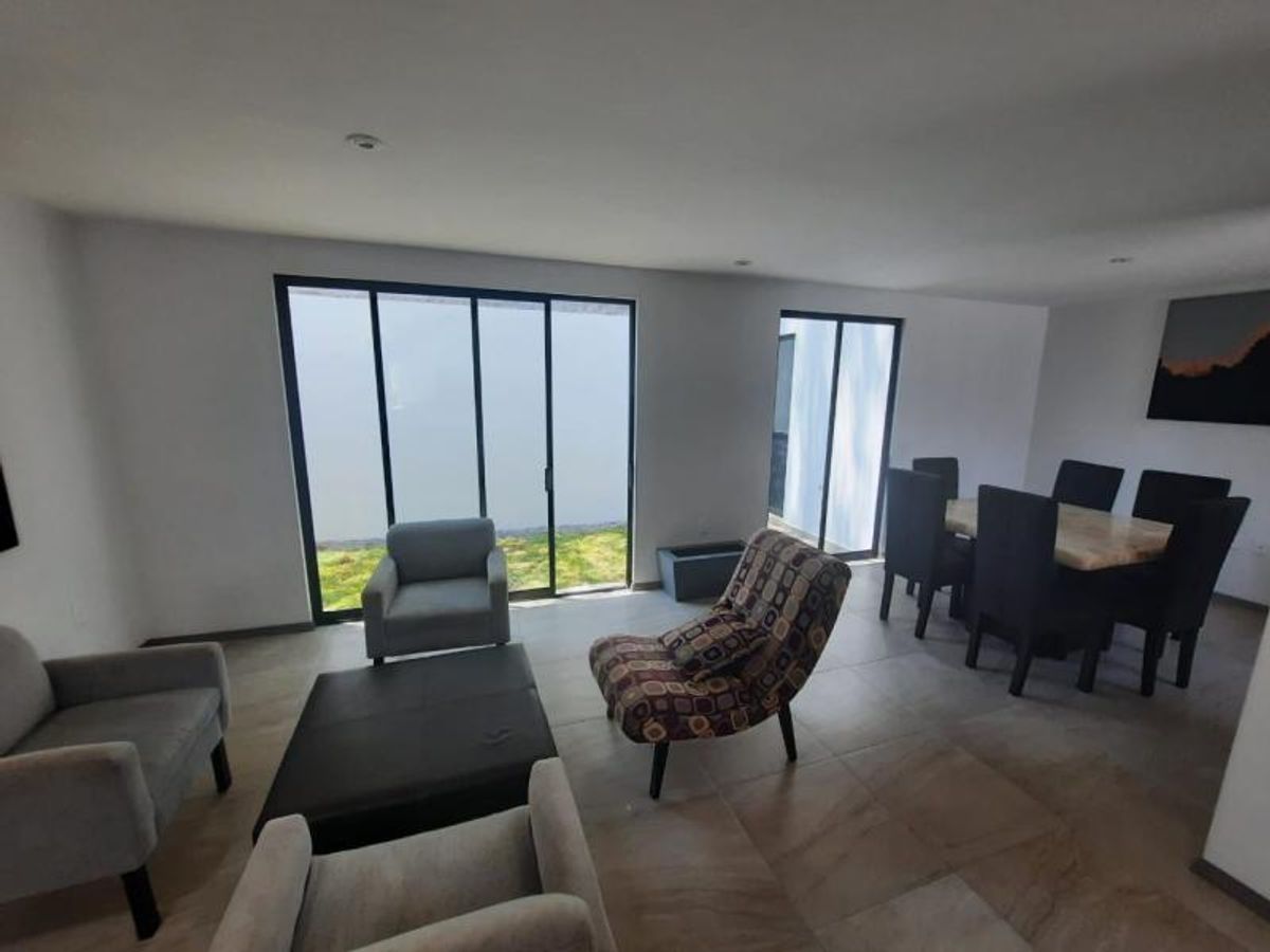 Sala y comedor con ventanales de piso a techo, sillones grises y mesa de centro