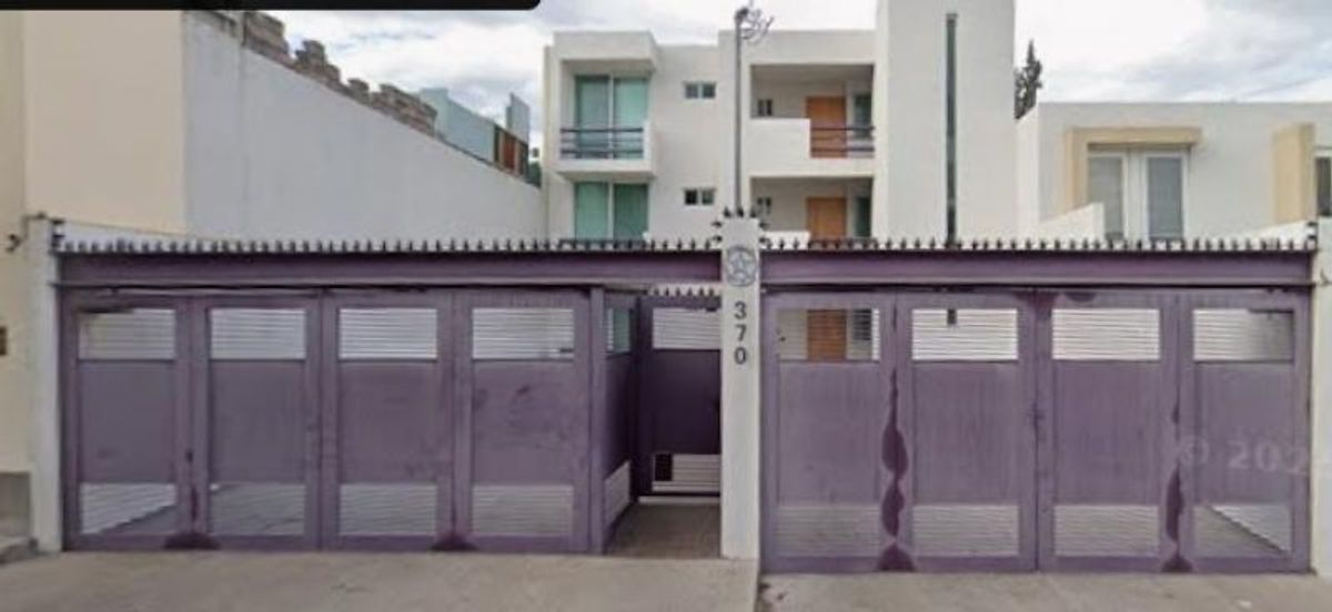 Fachada de edificio blanco de tres niveles con portón metálico morado en el acceso principal