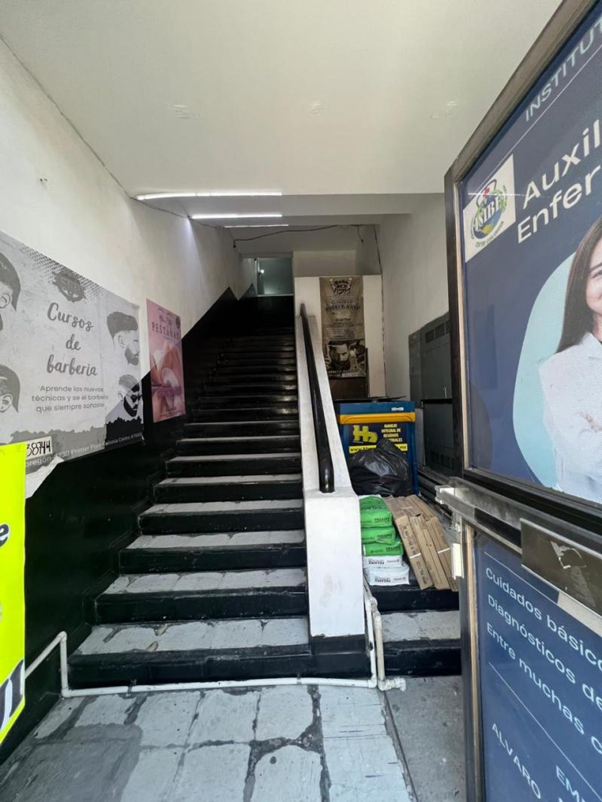 Pasillo de acceso con escaleras de peldaños negros, pasamanos y anuncios en los muros