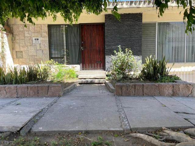Fachada frontal con puerta de madera, reja negra, muros de piedra y jardineras laterales