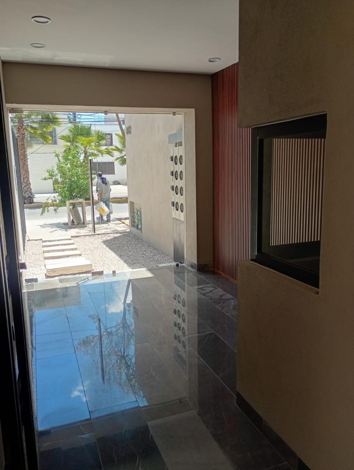Acceso principal con piso brillante reflectante, ventanales de cristal y muro decorativo con listones