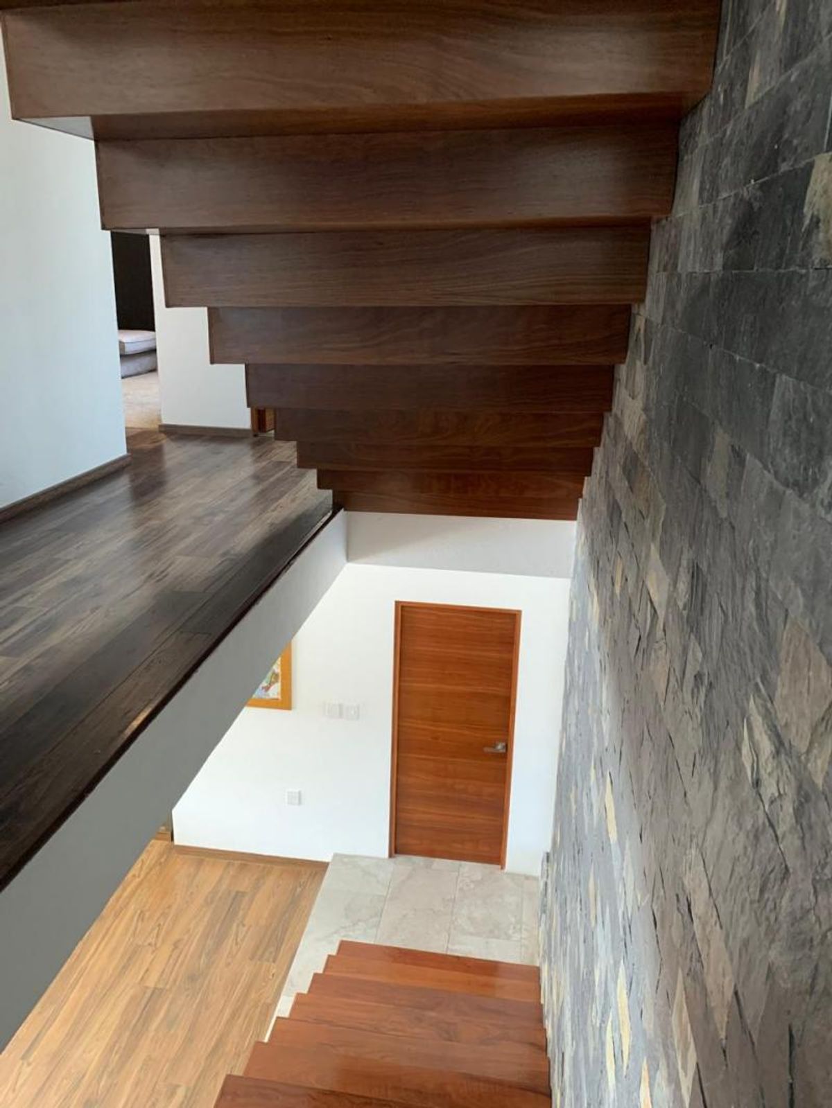 Escalera de madera con muro de piedra gris, pasillo y puerta de madera
