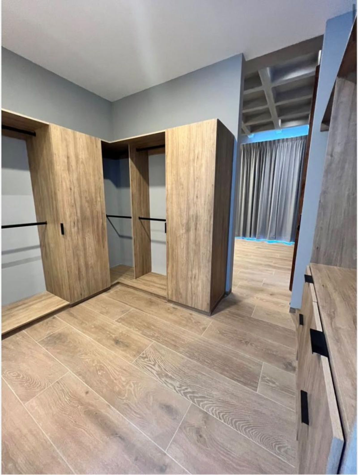 Vestidor de madera clara con barras metálicas para colgar y piso tipo madera