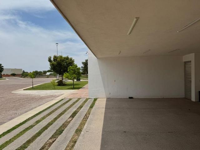 Cochera techada con piso de concreto y entrada con franjas de pasto al exterior