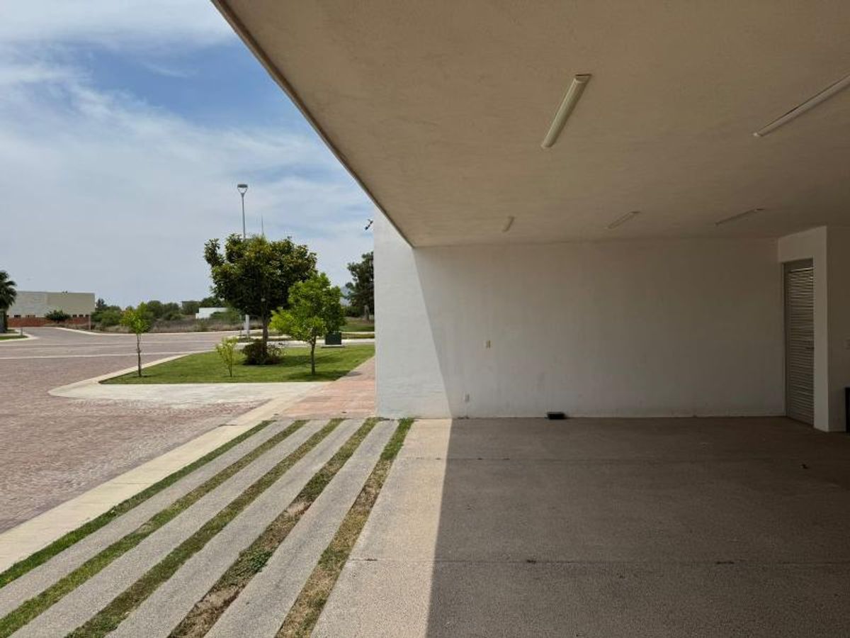 Cochera techada con muros blancos y entrada exterior con franjas de concreto y césped